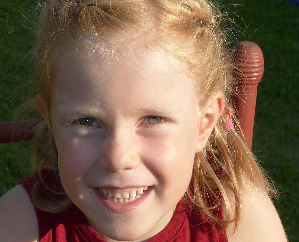 A young girl with blonde hair is smiling widely into the camera.
